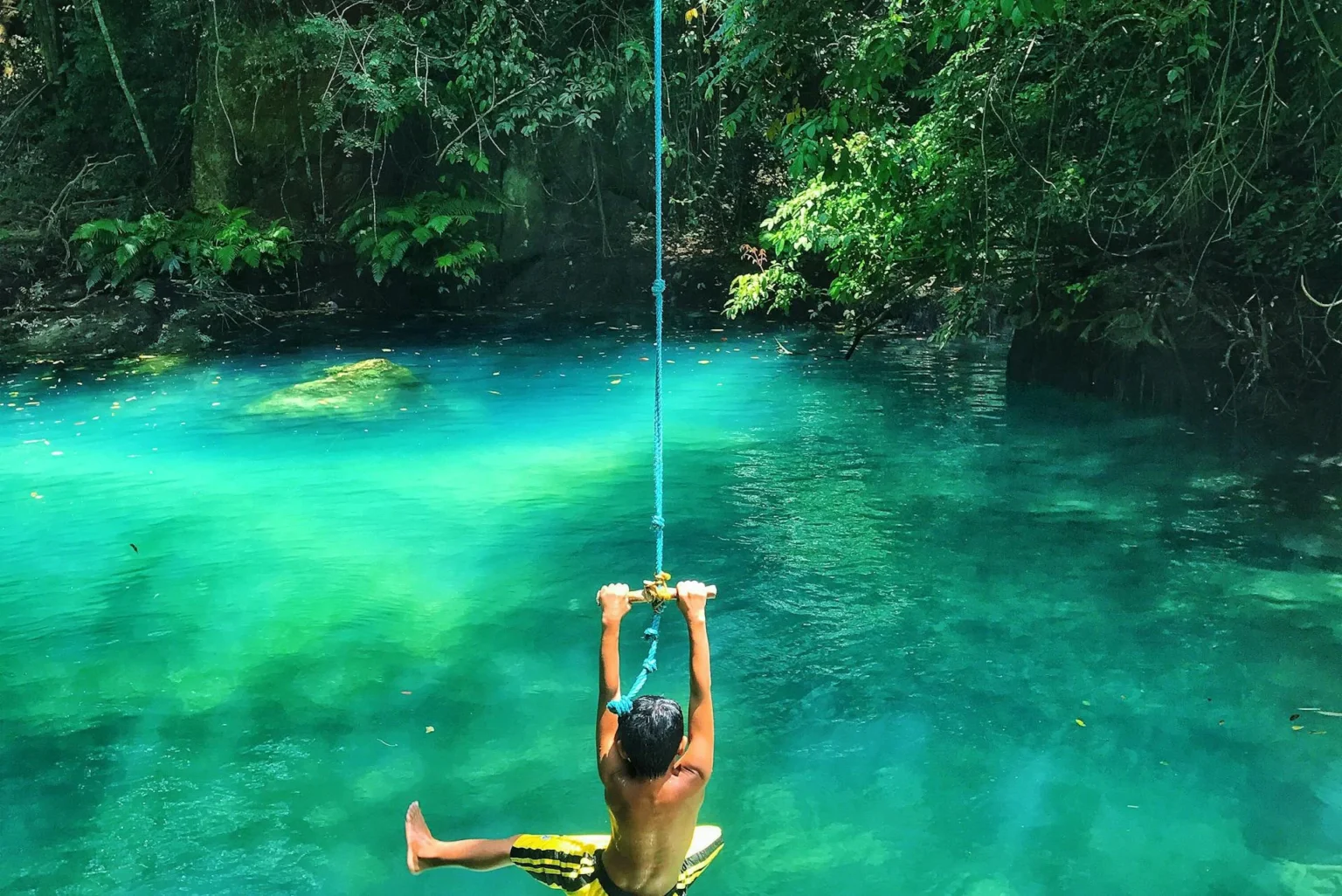 Child jump from line into blue lake in tropical forest